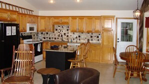 Una cocina con armarios de madera, un refrigerador negro, un microondas, una estufa y un comedor con sillas y una mesa de madera.