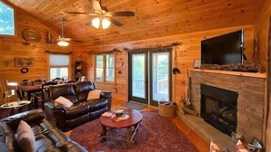 A cozy log cabin interior with a fireplace, leather sofa, and a television. - Big Rock Ridge - Easy Access for mountain views! (Murphy)
