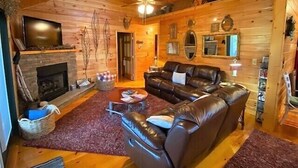 A cozy cabin interior with a fireplace, leather sofa, and wooden walls. - Big Rock Ridge - Easy Access for mountain views! (Murphy)