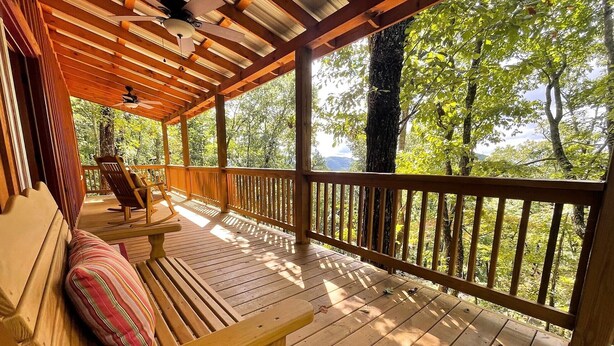 A wooden deck with a bench and chairs, overlooking a forested area. - Red Door Cabin - couples delight! (Murphy)