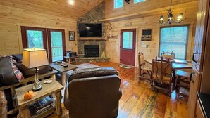 A cozy cabin interior with a fireplace, wooden floors, a dining area, and a ceiling fan. - Red Door Cabin - couples delight! (Murphy)