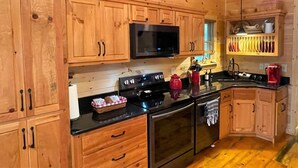A wooden-paneled kitchen with a microwave, stove, and oven. There are wooden cabinets and a countertop with various items. - Red Door Cabin - couples delight! (Murphy)
