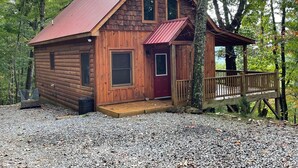 A wooden cabin with a red door, a porch, and a gravel driveway surrounded by trees. - Red Door Cabin - couples delight! (Murphy)