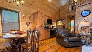 A cozy cabin interior with a dining area, a leather sofa, wooden floors, and a kitchen with wooden cabinets. - Red Door Cabin - couples delight! (Murphy)