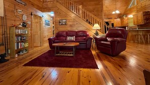 Ein gemütliches Cabin-Interieur mit einer Holztreppe, einem Wohnzimmer mit einem roten Sofa und Ledersesseln sowie einer Küchenzeile.