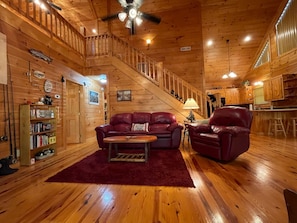 A cozy cabin interior with a wooden staircase, a living room with a red sofa and leather chairs, and a kitchen area. - Hemlock Heaven - wooded setting with easy access (Murphy)