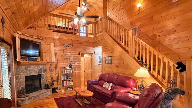 Ein gemütliches Blockhaus-Interieur mit Kamin aus Stein, einer Ledersofa und einer Treppe, die zu einer oberen Ebene führt.
