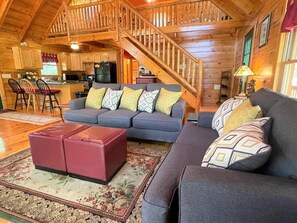 A cozy log cabin interior with a living room, kitchen, and a staircase.