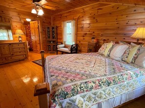 A wooden cabin bedroom with a large bed, a dresser, a chair, and a cabinet.
