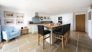 A modern kitchen with a central island, white cabinetry, and a dining area with black chairs.