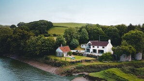 A coastal property with a main house and a smaller building, surrounded by lush greenery and a river.