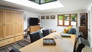 A modern kitchen with a skylight, wooden cabinets, a dining table with chairs, and a television.