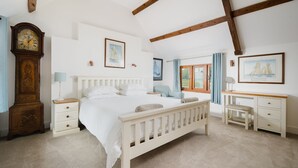 A bedroom with a large bed, a wooden dresser, a desk, and a wall-mounted clock.
