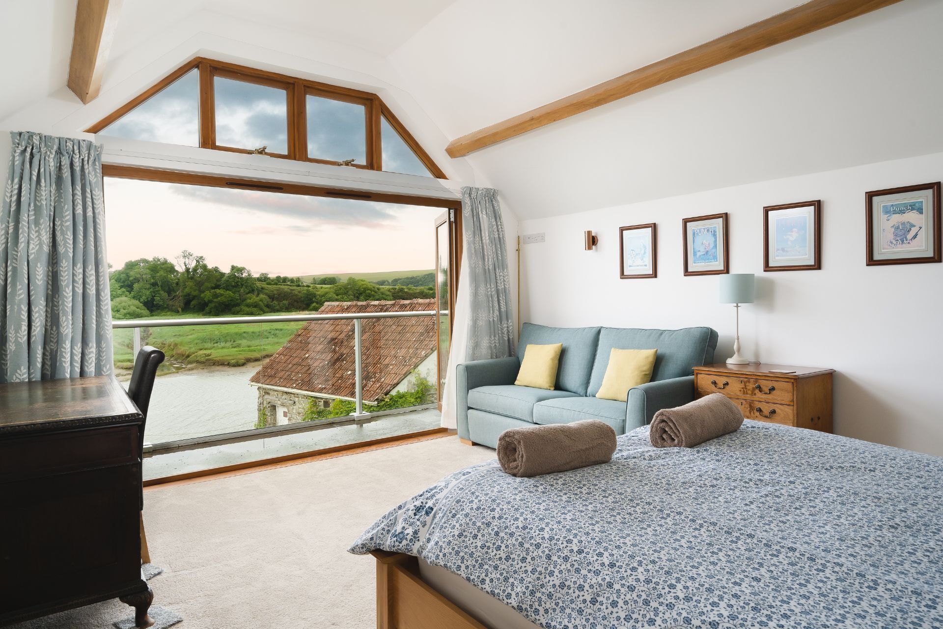 A bedroom with a large window, a sofa, a bedside table, and a bed.