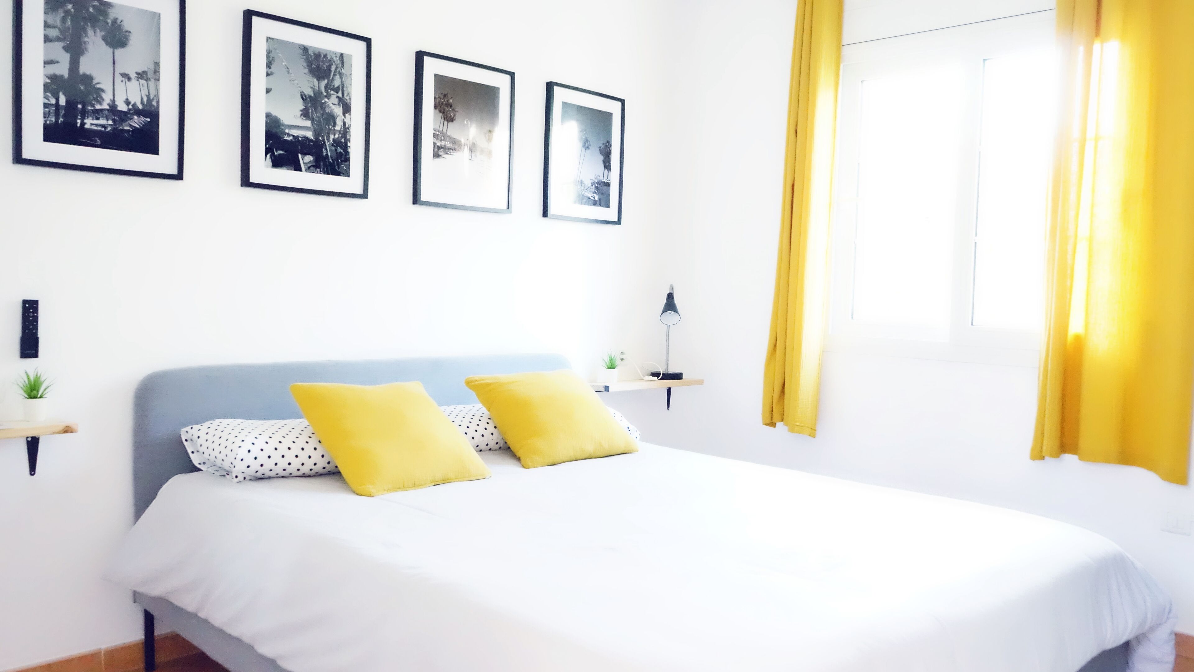 A bedroom with a bed, two pillows, a nightstand, a lamp, and three framed pictures on the wall.