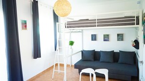 Une pièce avec un lit superposé, un canapé, une échelle, une lampe suspendue et une petite plante.