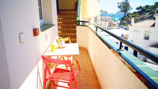 Un balcon avec une table et des chaises, une vue sur la rue et les immeubles, et un escalier menant à l’étage supérieur.