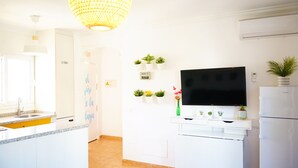 Une cuisine moderne avec des armoires blanches, un four encastré, un grand téléviseur à écran plat et un luminaire au plafond.