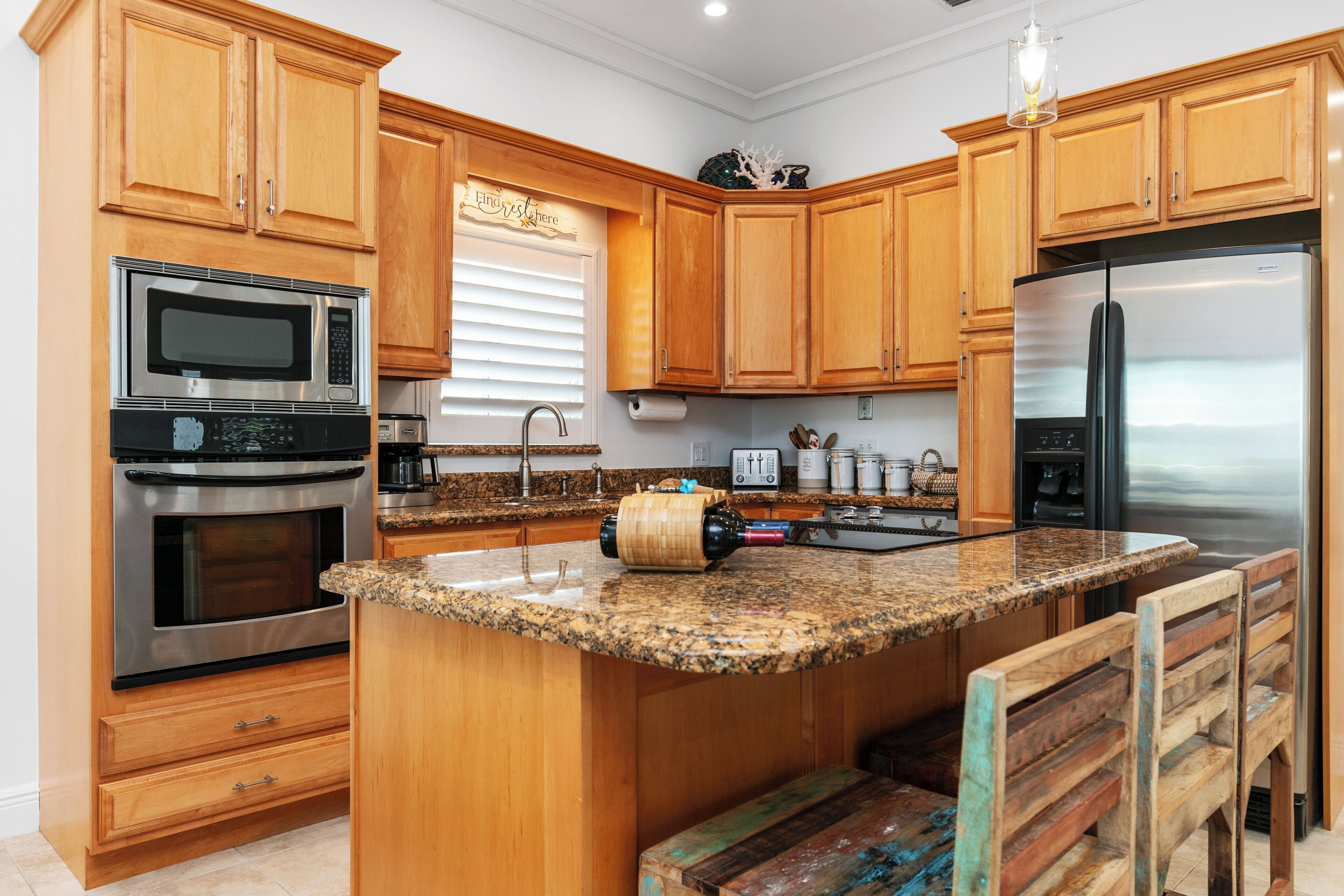 A kitchen with wooden cabinets, stainless steel appliances, a granite countertop, and a small island with a bench.