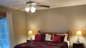 Ein Schlafzimmer mit einem hölzernen Bett, zwei Nachttischlampen, einem Deckenventilator und einem großen Fenster mit Vorhängen.