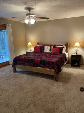 Una camera da letto con un letto in legno, due lampade sui comodini, una ventola a soffitto e un'ampia finestra con tende.