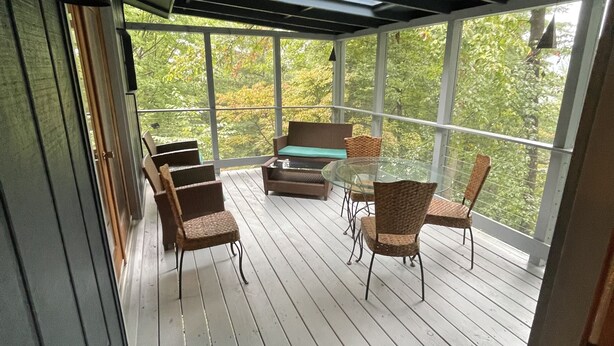 Eine überdachte Terrasse im Freien mit Holzboden, Korbmöbeln und einem Glastisch.