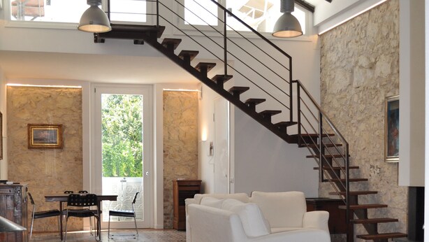 Ein geräumiger Wohnbereich mit Holzboden, einem weißen Sofa, einem Esstisch mit Stühlen und einer Treppe, die in eine obere Ebene führt.