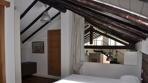 Ein Schlafzimmer mit schrägverdeckter Decke, einem Bett, einer Kommode und einem Fenster mit Vorhängen.
