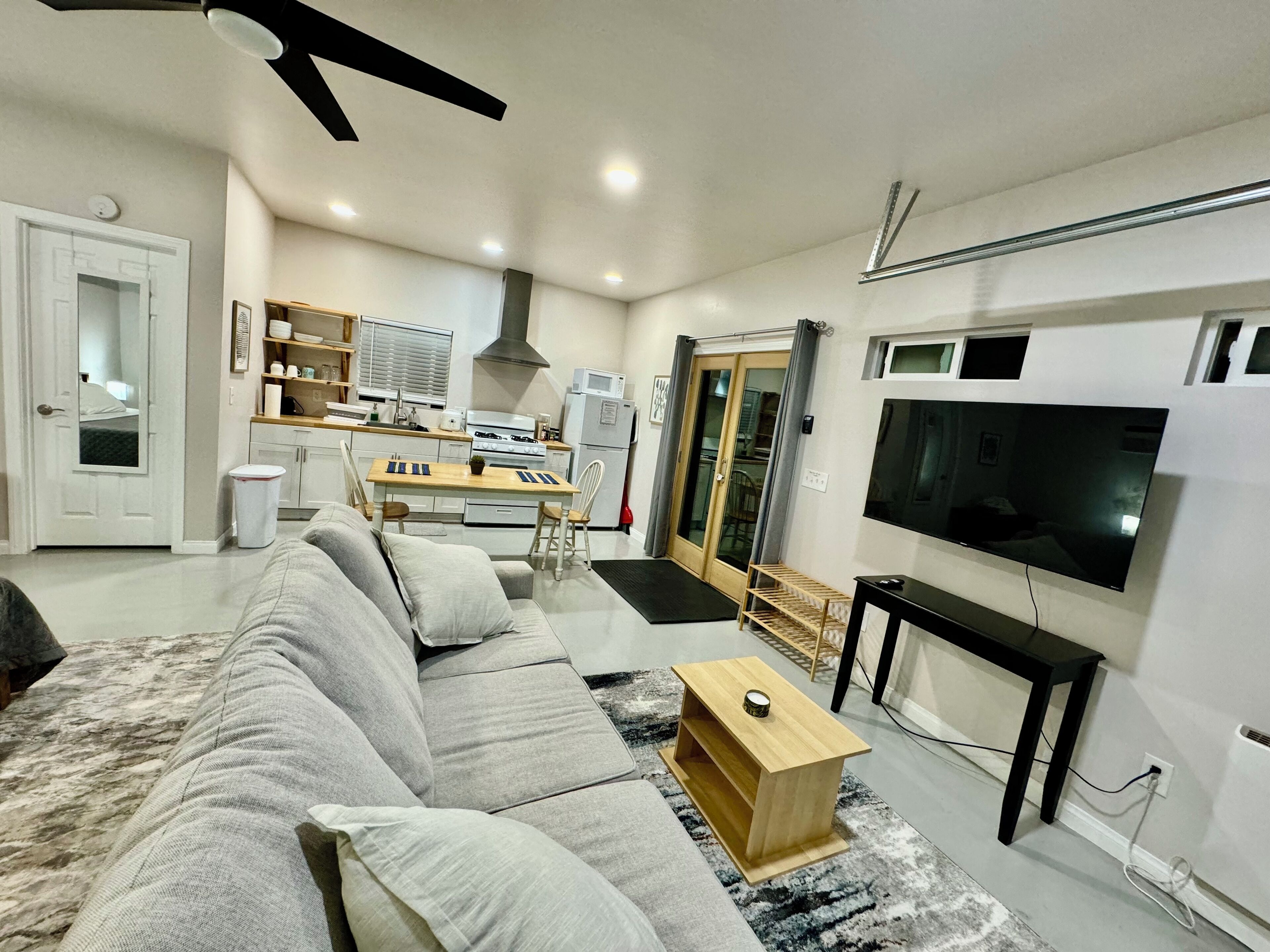 A modern living room with a grey sofa, a wooden coffee table, a TV, and a kitchen in the background.