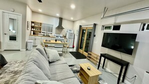 A modern living room with a grey sofa, a wooden coffee table, a TV, and a kitchen in the background. - Renovated studio 15 minutes from downtown San Diego (Lemon Grove)