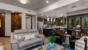 A modern living room with a gray leather sofa, a coffee table with decorative items, and a view of the kitchen and dining area. - Interior Design, Luxury Community Amenities, Free Shuttle + Pet-Friendly! (Park City)