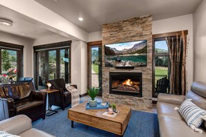A modern living room with leather sofas, a fireplace, and a large TV mounted on a stone wall.