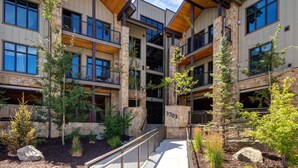 A multi-story building with stone and wood exterior, balconies, and a clear sky. - Interior Design, Luxury Community Amenities, Free Shuttle + Pet-Friendly! (Park City)