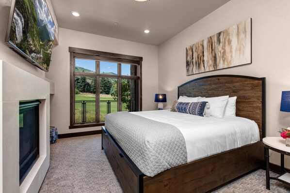 A bedroom with a large window, a bed, a TV, and a fireplace.