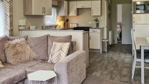 A modern living room with a beige sofa, a small white table, and a kitchen area with cabinets and appliances. - Castle Campbell View (Dollar)