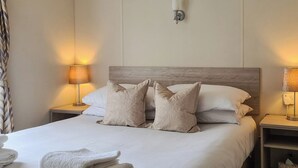 A neatly made bed with a wooden headboard, two bedside lamps, and a wall-mounted light fixture. - Castle Campbell View (Dollar)