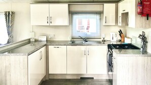 A compact kitchen with white cabinets, a built-in stove, and a window with blinds. - Castle Campbell View (Dollar)