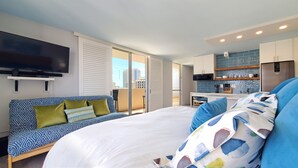 Une chambre d’hôtel moderne dotée d’un grand lit, d’un canapé, d’une télévision, d’un balcon offrant une vue sur la ville et d’une kitchenette.