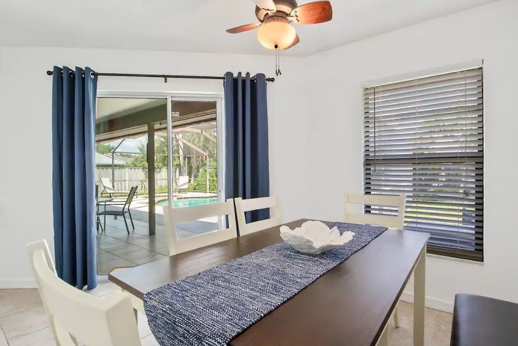 A dining area with a table, chairs, a ceiling fan, and a view through a glass door to an outdoor patio.