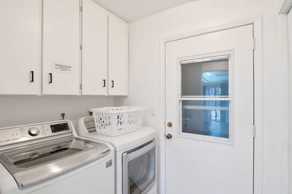 A laundry room with a front-loading washer and dryer, a white door with a window, and a basket on the dryer.