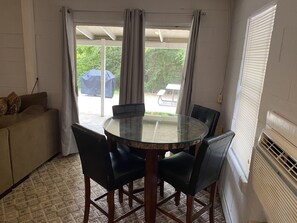 A room with a glass-top table surrounded by chairs, a sofa, and a sliding glass door leading to an outdoor area with a covered table. - Waterfront with Sandy Shores! (Eufaula)