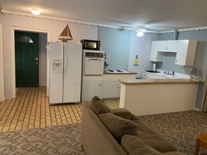 A compact kitchen with a refrigerator, microwave, oven, and sink. There is a green door and a patterned rug on the floor. - Waterfront with Sandy Shores! (Eufaula)