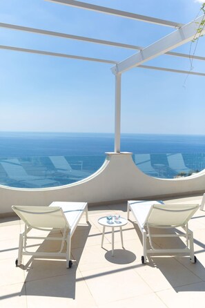 A terrace with two white lounge chairs and a small table, overlooking a clear blue sea and distant buildings. - Casa Blue Star in Praiano (Praiano)