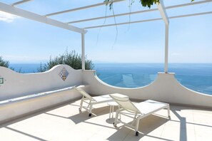 A sunlit outdoor seating area with a clear view of the sea, white furniture, and a tiled floor. - Casa Blue Star in Praiano (Praiano)