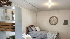 A small, cozy bedroom with two beds, a wooden floor, a white wall, and a round wall clock.