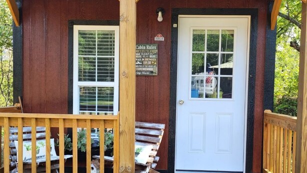 A cabin with a wooden deck, a white door, and a sign listing cabin rules.