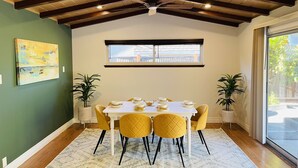 Un comedor con una mesa dispuesta para cuatro, vigas de madera en el techo, una ventana con vistas y dos plantas en macetas.