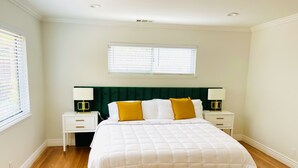 Un dormitorio con una cama grande, dos mesitas de noche, dos lámparas, una ventana con persianas y un cabecero verde.