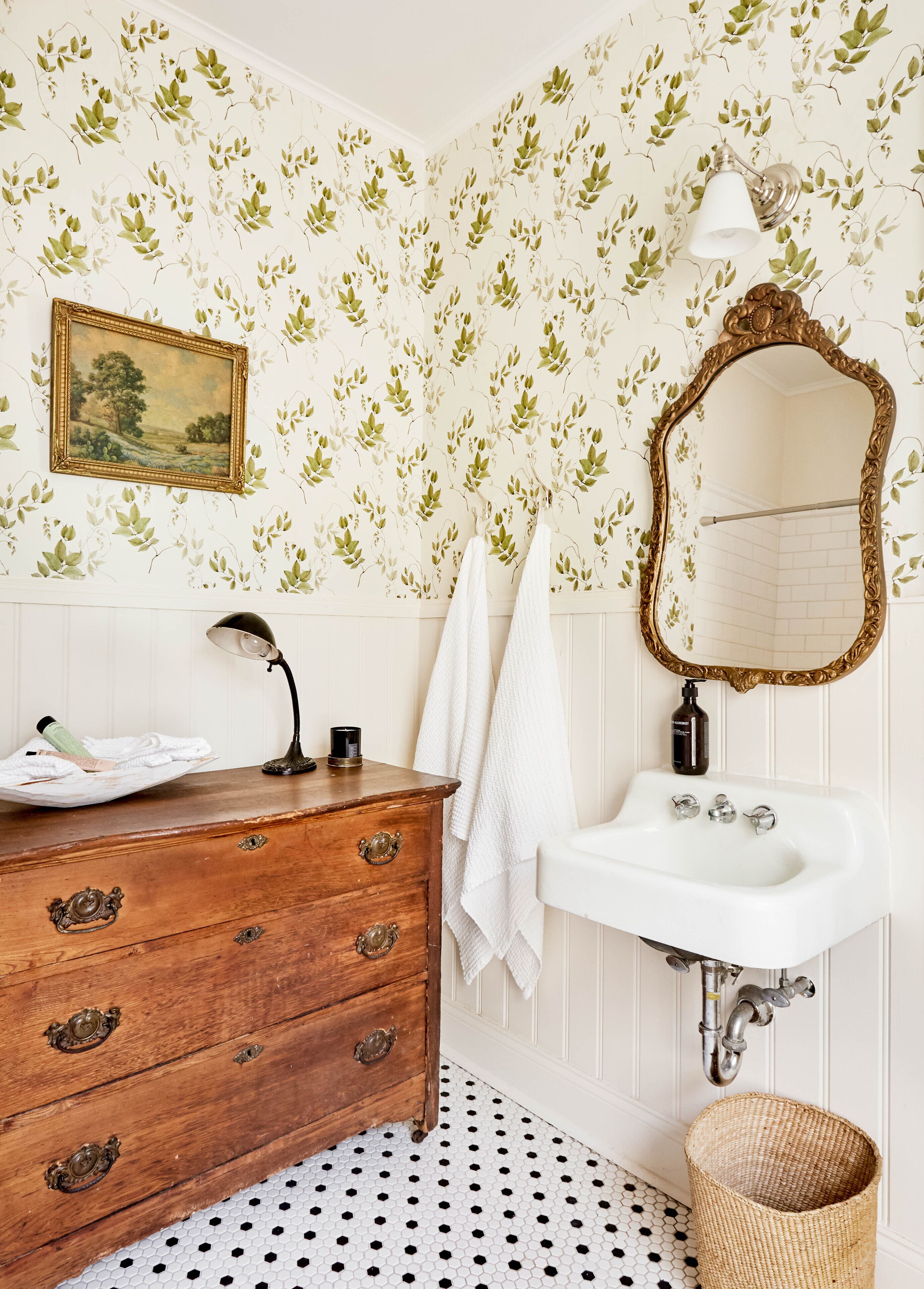 Un baño con cómoda de madera, lavamanos blanco y espejo con marco decorativo.