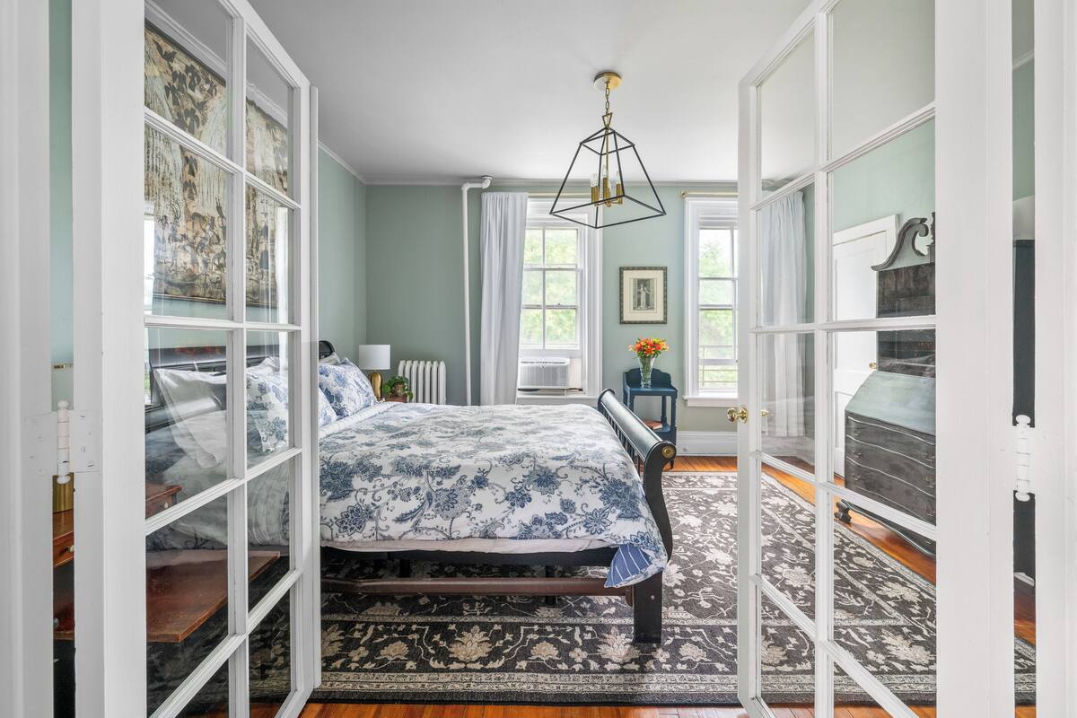 A bedroom with a bed, a nightstand, a dresser, and a window with curtains.
